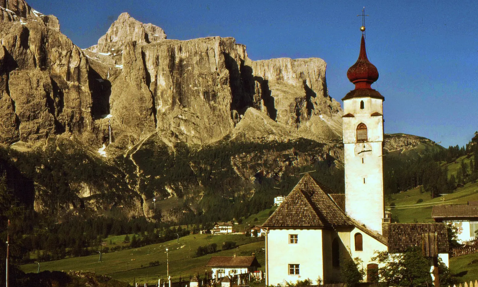 Iglesia blanca con campanario de bulbo rojo al pie de las paredes de los Dolomitas.